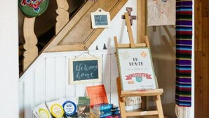 A wooden staircase with colorful flags, a welcome sign, a small easel with a sign, and a basket of books and snacks. - Maison la Gileppe (Jalhay)