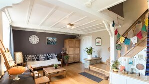 A cozy living room with a sofa, coffee table, and a staircase with colorful flags. - Maison la Gileppe (Jalhay)