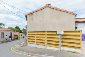 A building with a beige exterior and a tiled roof, a yellow fence, and a street with pedestrians.