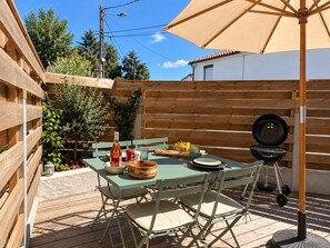 An outdoor patio with a wooden table, chairs, a barbecue grill, and a large umbrella.