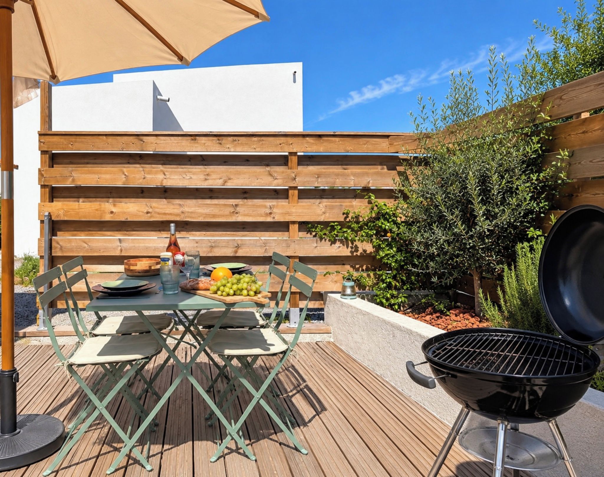 Une terrasse extérieure avec une table dressée pour le repas, un barbecue et une clôture en bois en arrière-plan.
