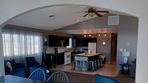 A modern kitchen with dark cabinets, a central island with stools, and a dining area with a table and chairs. - Alexander’s Landing Penthouse - Lakefront, Balcony, and Room to Relax (Monticello)
