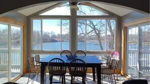 A sunroom with a large window overlooking a lake, a dining table with chairs, and a ceiling fan. - Alexander’s Landing Penthouse - Lakefront, Balcony, and Room to Relax (Monticello)