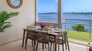 A dining area with a table set for four, a large window with a view of the sea, and a potted plant on the left. - Lagoon view & Sunset ! Full unit 2BDR 2,5BTH (SAINT MARTIN)