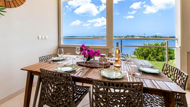 A dining table set for four with a view of the sea through large windows. - Lagoon view & Sunset ! Full unit 2BDR 2,5BTH (SAINT MARTIN)