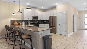A modern kitchen with white cabinets, a large island with bar stools, stainless steel appliances, and pendant lighting.