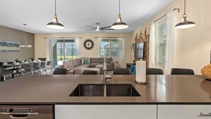 A modern kitchen with a central island, pendant lights, and a ceiling fan.