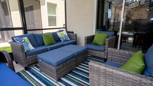 A sunlit outdoor seating area with wicker furniture and striped rugs. - Luxury 6BR Retreat w/ Pool, Spa & Walk to Clubhouse! (Kissimmee)