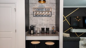 A modern kitchen with a coffee bar, including coffee makers and a sign. There are two stools under the bar. - Luxury 6BR Retreat w/ Pool, Spa & Walk to Clubhouse! (Kissimmee)