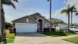A residential house with a white garage door, a driveway, and a well-maintained lawn with palm trees. - 4BR Pool Home at Lake Berkley (Kissimmee)