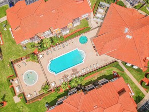 An aerial view of a property with a swimming pool, lounge areas, and a circular fountain.