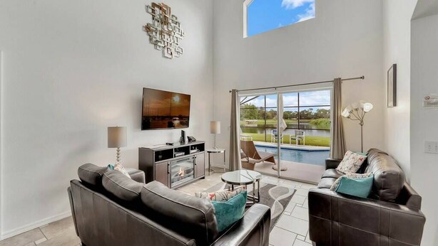 A spacious living room with a fireplace, a television, and a view of a pool through large sliding glass doors. - Lakeview Retreat with Private Pool & Games (Kissimmee)