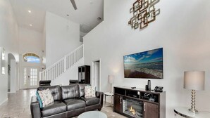 A modern living room with a fireplace, a large flat-screen TV, and a staircase leading to an upper level. - Lakeview Retreat with Private Pool & Games (Kissimmee)