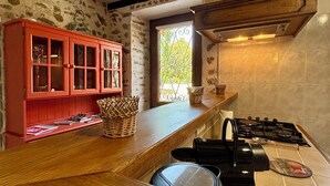 A kitchen with a wooden countertop, a red cabinet, a gas stove, and a window with a view of trees.