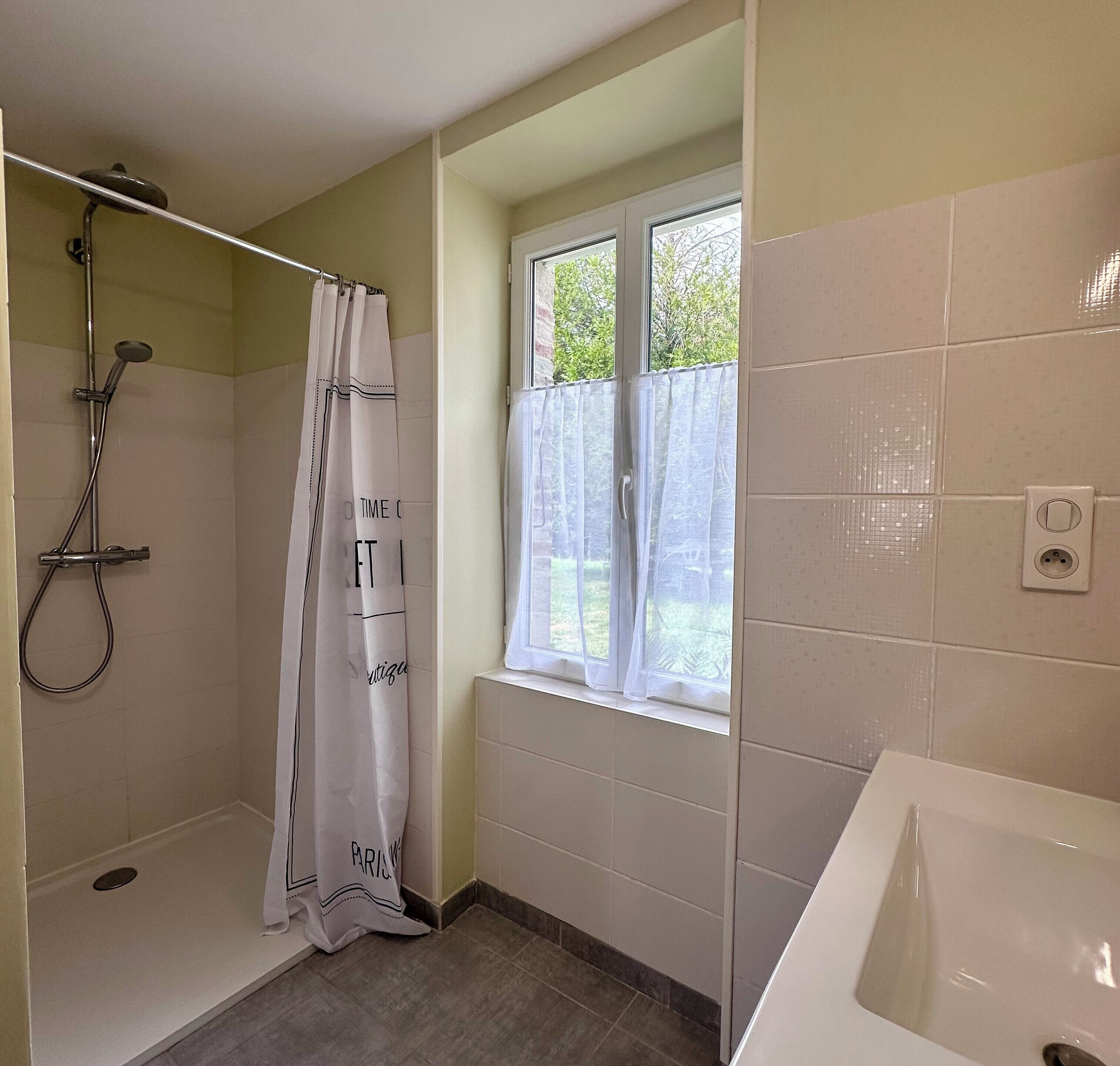 A bathroom with a shower, a window with curtains, and a bathtub.