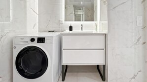 Un baño moderno con lavadora incorporada, un tocador blanco con cajones y un espejo grande sobre el lavabo.