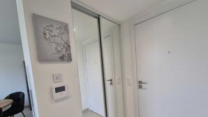 Una habitación moderna con una puerta de cristal corredera que da a un pasillo, una pequeña mesa con sillas y un termostato fijado a la pared.