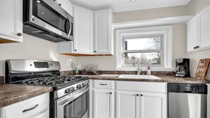 Une cuisine moderne avec des meubles blancs, des appareils en acier inoxydable, un plan de travail en granit et une fenêtre offrant une belle vue.