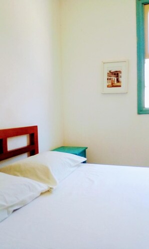 Una habitación sencilla con una cama, una mesita pequeña y un cuadro enmarcado en la pared.