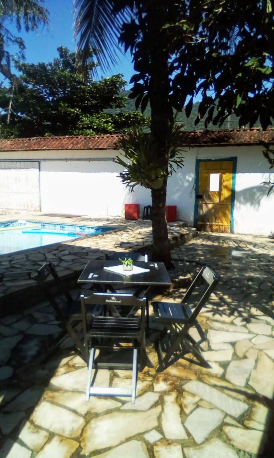 An outdoor area with a pool, stone flooring, a table with chairs, and a palm tree.