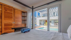A hotel room with a large bed, wooden wardrobe, and a view of a swimming pool and outdoor seating area. - Palm Villa 4BR Luxe pool retreat (Sosúa)