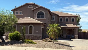 A two-story house with a stone foundation, a large arched window, and a covered patio area. - Relax in the Gilbert Getaway (Gilbert)