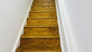 A wooden staircase with white walls and a potted plant at the top.