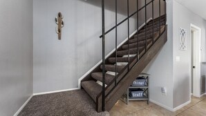A staircase with a wooden handrail and carpeted steps, leading to a landing with a white door and a small shelf with labeled boxes.