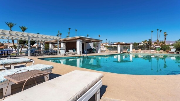 A pool area with lounge chairs, a covered seating area, and palm trees.