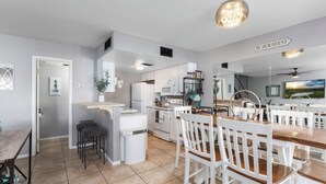 A modern kitchen with white cabinets, a central island, and a dining area with white chairs.