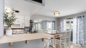 A modern kitchen with white cabinets, a wooden countertop, and a dining area with white chairs.
