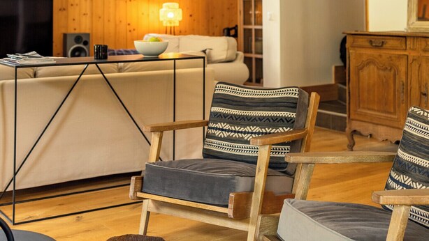 A cozy living room with wooden walls, a TV, a sofa, and a dining area. - Chalet Achillée – 5 Bedrooms (Les Allues)