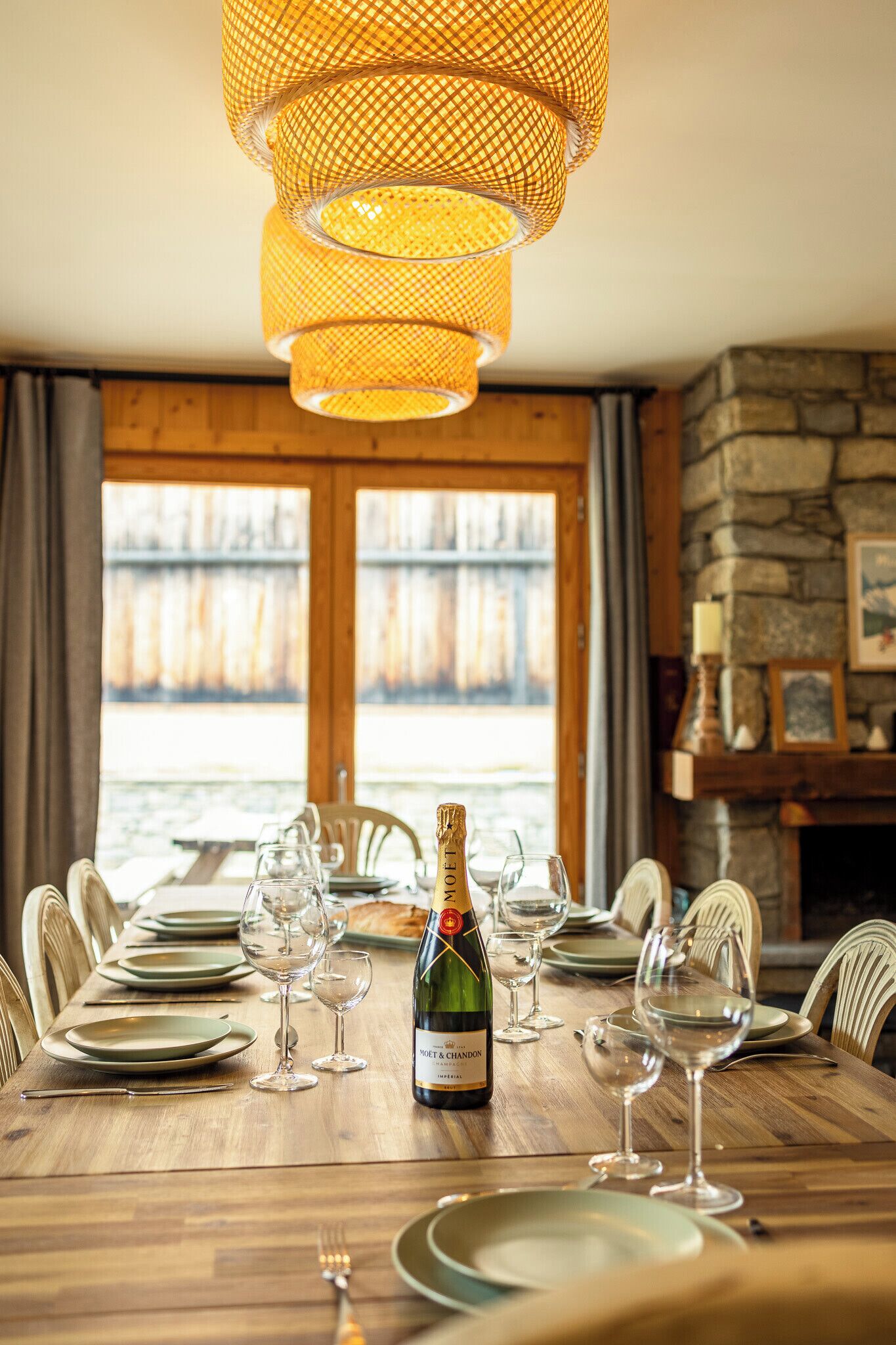 Mesa de comedor lista para seis personas, con copas de vino, platos y una botella de vino.