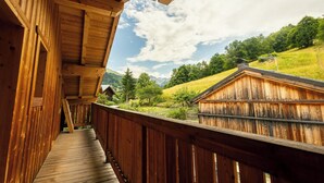 A wooden deck with a view of a rural landscape, including a house and mountains. - Chalet Achillée – 5 Bedrooms (Les Allues)