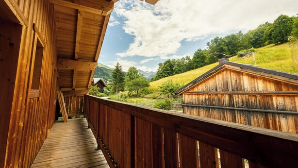 Une terrasse en bois offrant une vue sur un paysage rural, avec une maison et des montagnes en toile de fond.