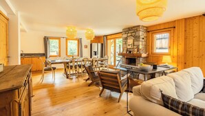 A spacious living area with a dining table, chairs, a sofa, and a stone fireplace. - Chalet Achillée – 5 Bedrooms (Les Allues)