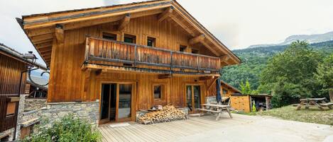 A wooden chalet with a balcony, stone foundation, and a view of the surrounding forest.