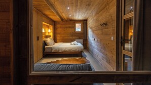 A narrow, wooden-paneled room with a bed, a small window, and a door. - Chalet Achillée – 5 Bedrooms (Les Allues)