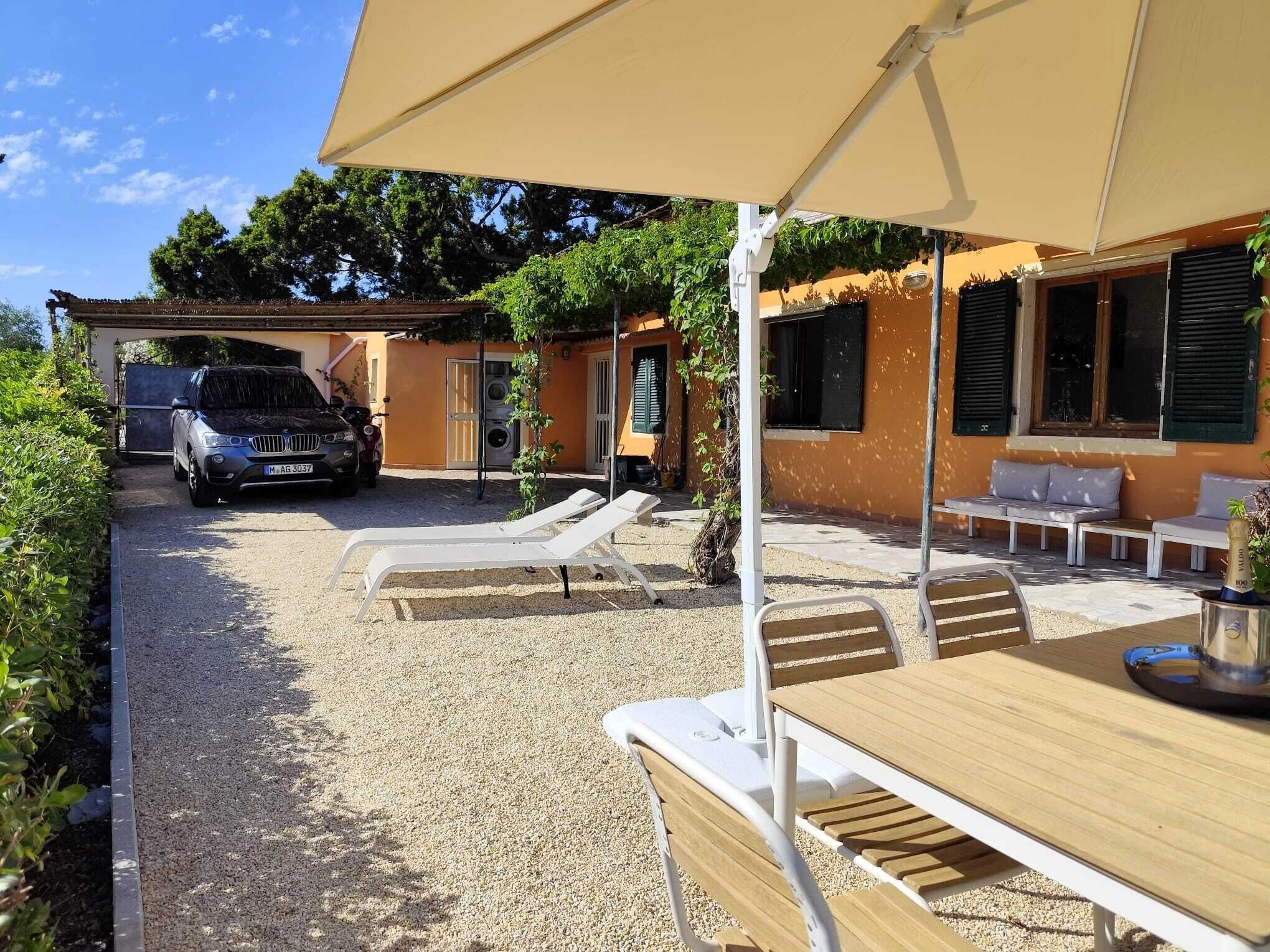 A covered outdoor seating area with tables and chairs, a car parked in the background, and a building with a yellow facade.