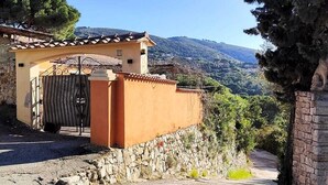 A building with a stone wall, a metal gate, and a view of a hilly landscape.