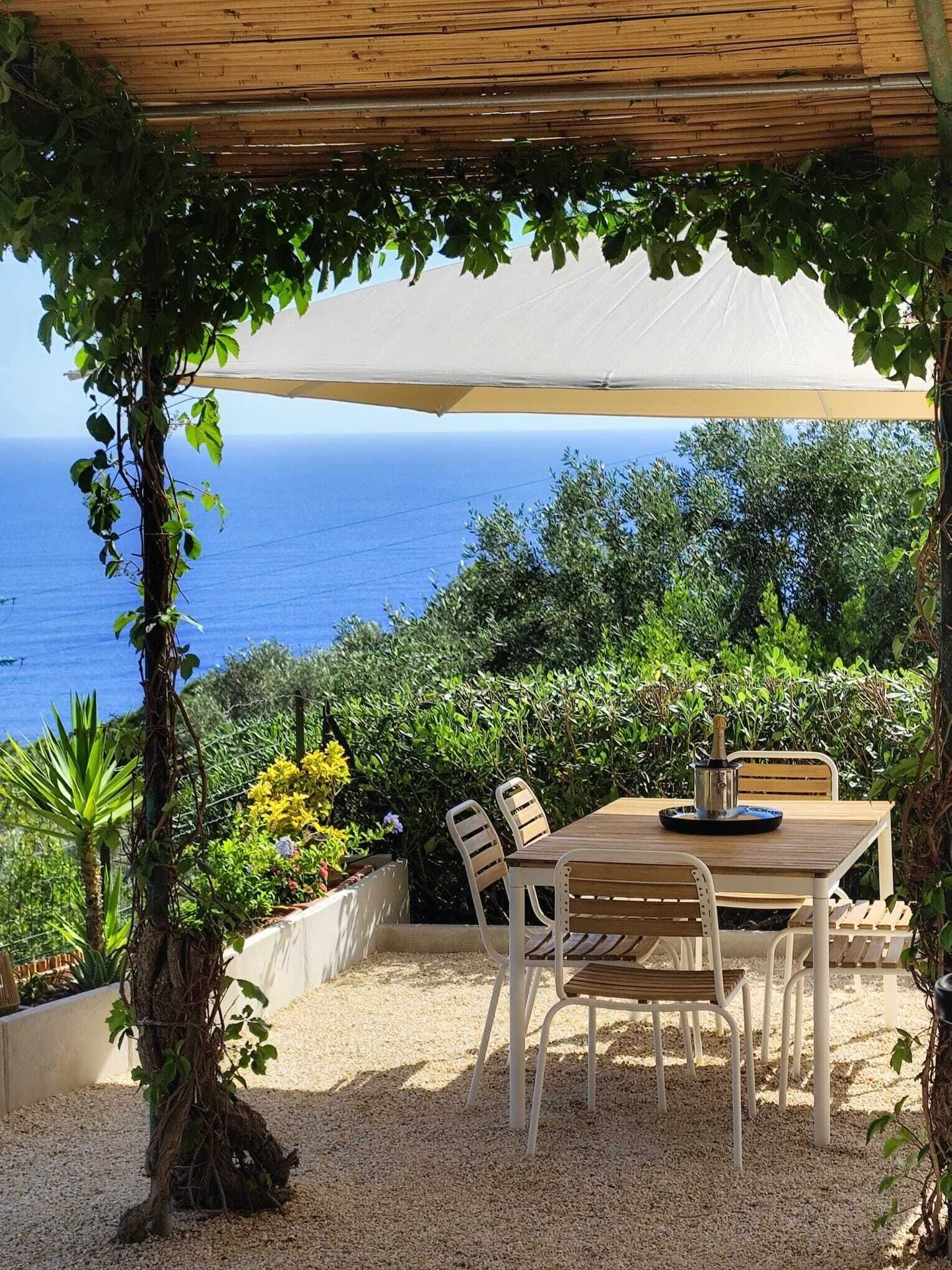 A covered outdoor dining area with a table and chairs, overlooking the sea.