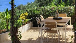 A covered outdoor dining area with a table and chairs, overlooking the sea.