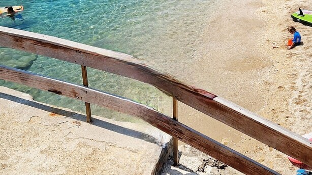 A beach with clear water, rocky shore, and a wooden railing.