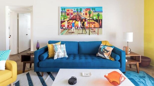 A living room with a blue sofa, a white coffee table, and a colorful painting on the wall.