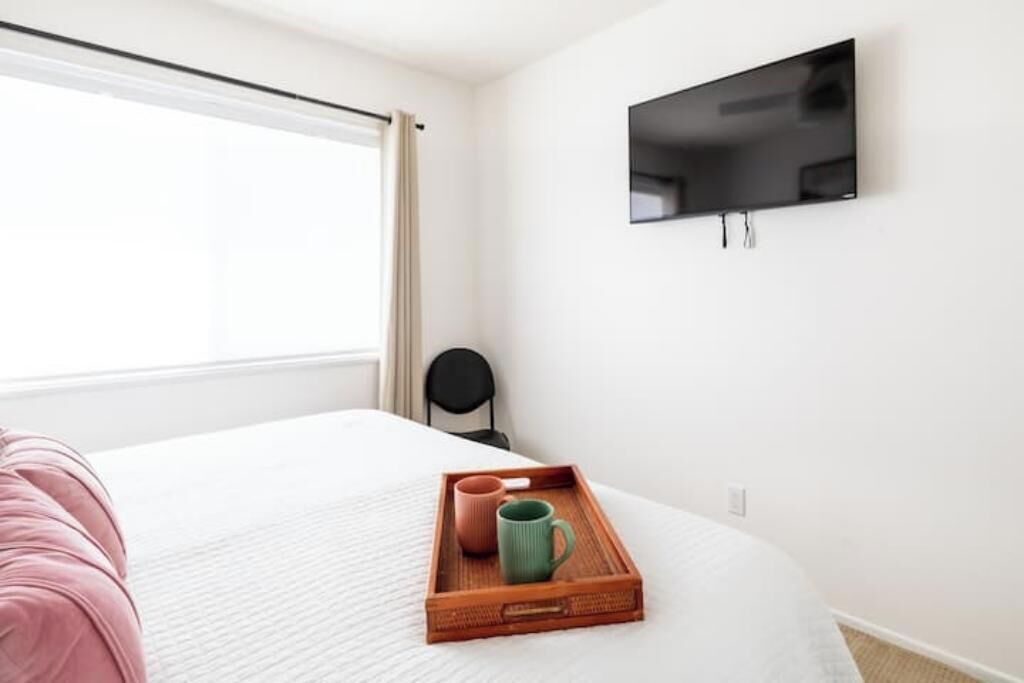 A hotel room with a bed, a TV mounted on the wall, and a window with curtains.