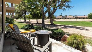 A patio with outdoor furniture, a round table, and a view of a golf course and buildings in the distance.