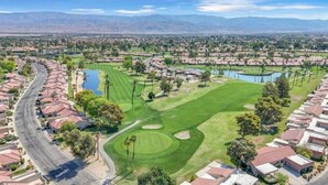 A golf course with a water hazard, surrounded by residential areas and mountains in the background.