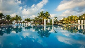 Una piscina con palmeras y chozas de techo de paja, rodeada por un cielo despejado.