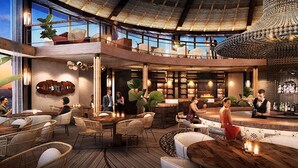 Un espacio interior amplio con techos altos, mobiliario de mimbre y una zona de bar con gente.