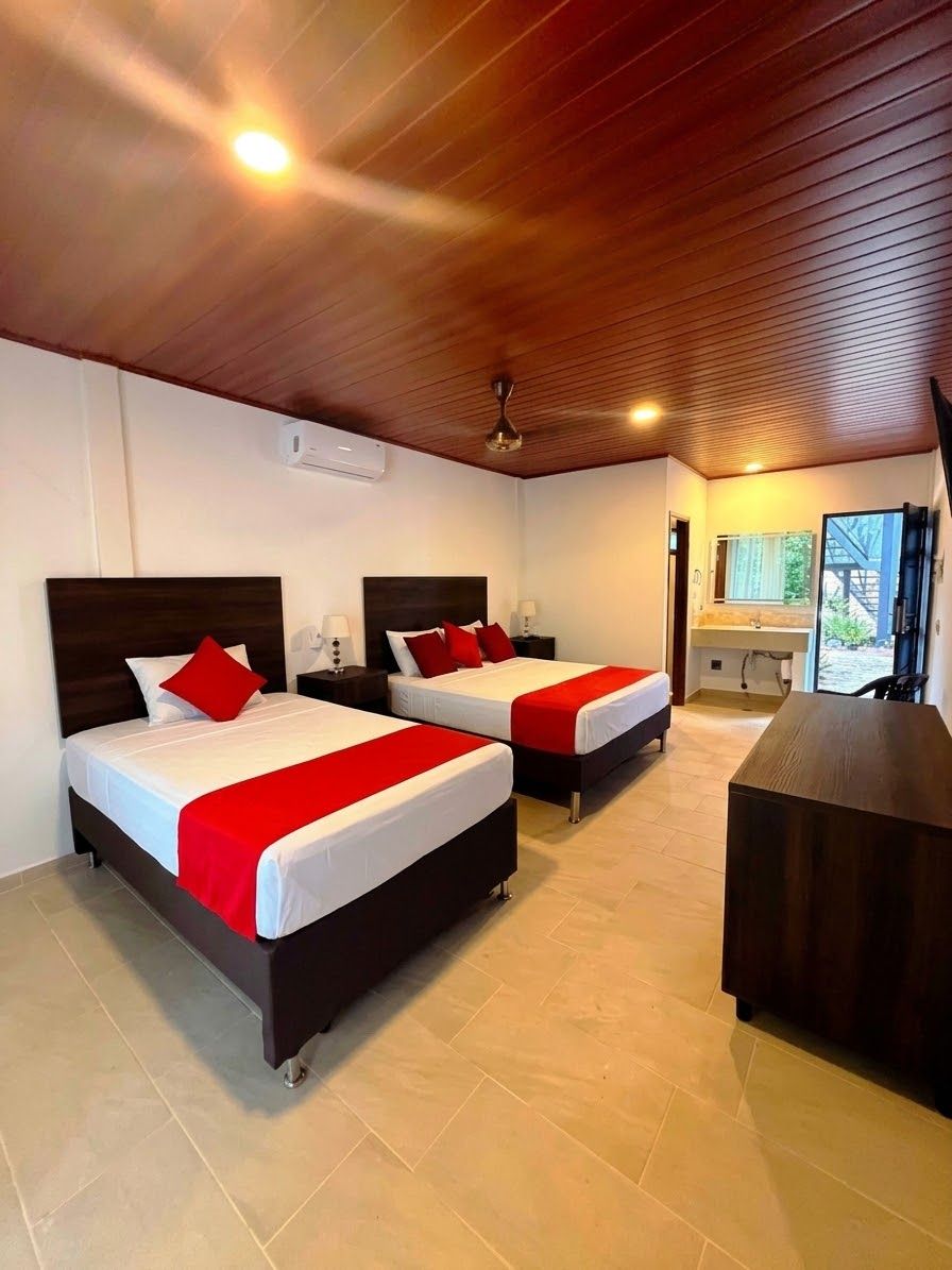 Habitación de hotel con dos camas, un escritorio y un baño visible a través de una puerta abierta.